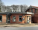 Ristorante La Stazzione Es ist ein runder Backsteinbau direkt am Meldorfer Bahnhof. Im Hintergrund sind hohe Bäume zu sehen.